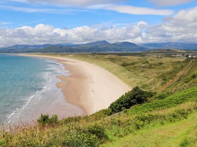 A sandy beach with sea on the left and grassy dunes on the right with mountains in the background at Glyn Morfa in Harlech