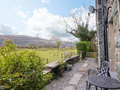 A garden area with stone wall, table, chairs and plants at Glyn Morfa in Harlech