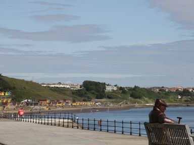 A seaside promenade with a bench and statue overlooking the beach and colorful beach huts at The Sequoia in Cloughton