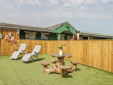 An outdoor area with two lounge chairs a wooden table with stools a wooden fence and a horse behind the fence at The Sequoia in Cloughton