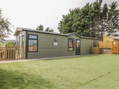 A green mobile home with black framed windows and wooden fencing on a lawn at The Sequoia in Cloughton