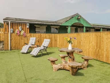 An outdoor area with two striped lounge chairs a wooden table with attached stools and a wooden fence with flower pots at The Sequoia in Cloughton