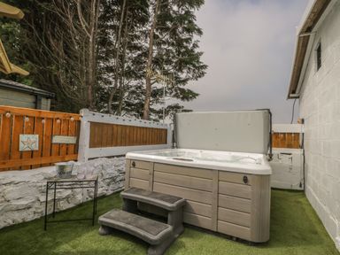 An outdoor space with a hot tub and small table with glasses and a bucket next to a wooden fence