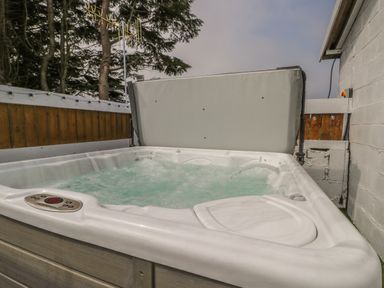 An outdoor hot tub with bubbling water surrounded by wooden fence and concrete wall at The Sequoia in Cloughton