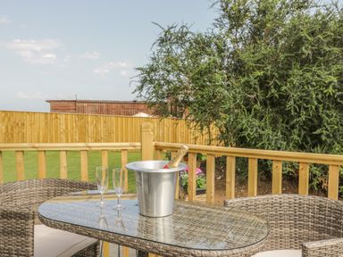 An outdoor patio with a glass table and wicker chairs with a bottle in an ice bucket and two glasses at The Sequoia in Cloughton