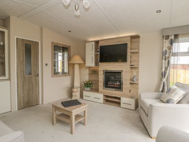 A living room with a wall-mounted TV and electric fireplace a wooden coffee table a floor lamp a large mirror and a sofa at The Sequoia in Cloughton