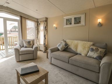 A living room with a beige sofa and armchair with cushions a wooden coffee table and framed artwork at The Sequoia in Cloughton