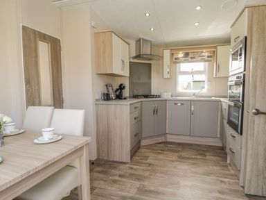 A kitchen with grey cabinets, built-in oven, microwave, stove, dining table with two chairs and cups at The Sequoia in Cloughton