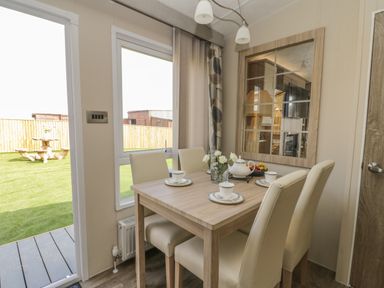 A dining area with a wooden table set with white cups and plates four chairs and a large window showing a backyard at The Sequoia in Cloughton