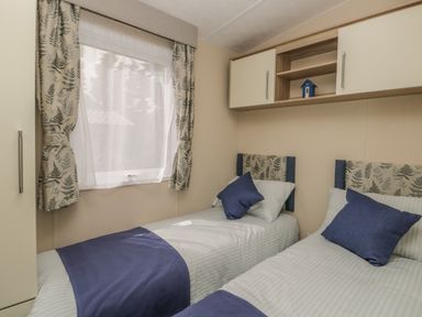 A bedroom with two single beds with patterned headboards and blue pillows under a window with patterned curtains at The Sequoia in Cloughton