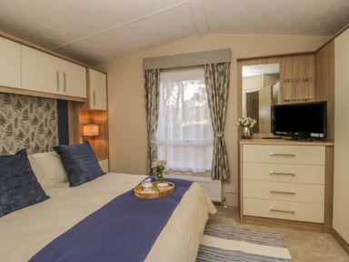 A bedroom with a bed with blue and beige bedding a window with curtains and a dresser with a TV and flowers at The Sequoia in Cloughton