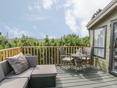 An outdoor deck with a sectional sofa and a small table with two chairs and a bucket with a bottle at The Maple in Cloughton