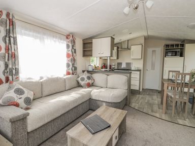A living room with an L-shaped sofa and patterned curtains next to an open kitchen and dining area at The Maple in Cloughton