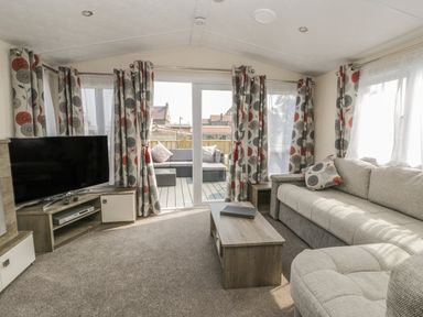 A living room with a sofa a coffee table a television and curtains on windows at The Maple in Cloughton