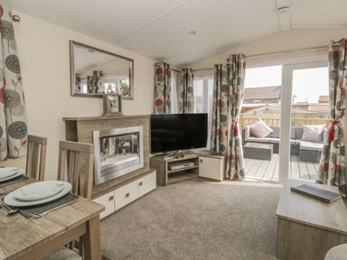 A living room with a fireplace television dining table and sliding doors leading to a patio at The Maple in Cloughton