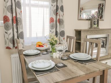 A dining room with a wooden table set with plates glasses and cutlery near a window with patterned curtains at The Maple in Cloughton