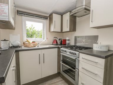 A kitchen with a stove, sink, red kettle, red toaster, and cabinets at The Maple in Cloughton