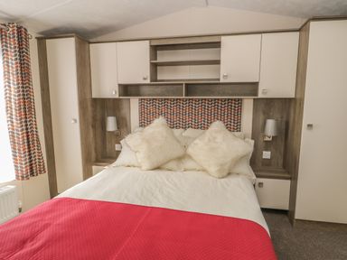 A bedroom with a bed with white and red bedding and built in storage at The Maple in Cloughton