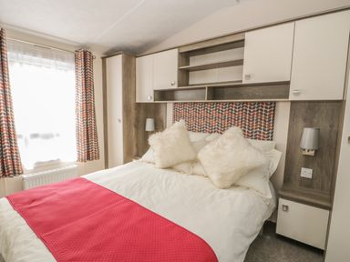 A bedroom with a bed with white bedding and red runner and cabinets above the headboard at The Maple in Cloughton