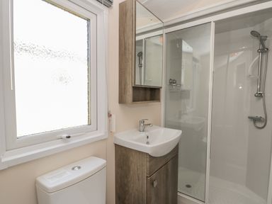 A bathroom with a toilet under a window a wooden vanity with a sink a mirrored cabinet and a glass shower enclosure at The Maple in Cloughton