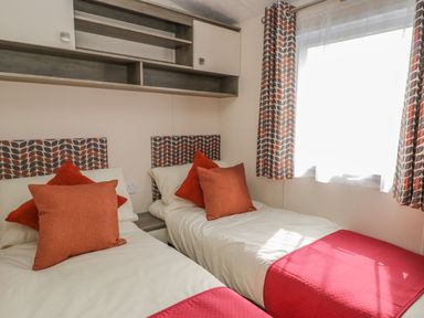 A bedroom with two single beds with patterned headboards orange pillows and matching curtains at The Maple in Cloughton
