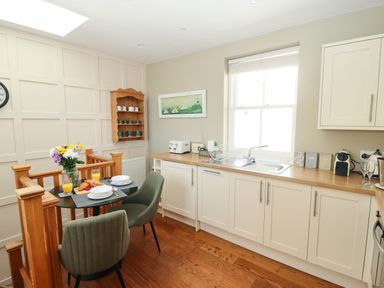 A kitchen with white cabinets a wooden countertop green chairs and a small dining table with breakfast items at Gavel Cottage in Whitby