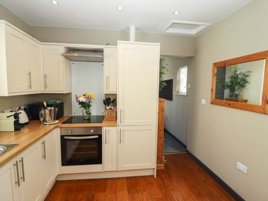 A kitchen with white cabinets a built in oven a vase of flowers and a wooden floor at Gavel Cottage in Whitby