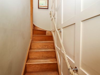A wooden staircase with a rope handrail and paneled wall at Gavel Cottage in Whitby