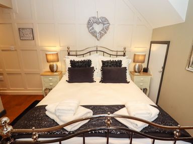 A bedroom with a double bed with white linens and black pillows with two bedside tables with lamps at Gavel Cottage Whitby