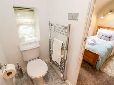 A small bathroom with a toilet towel radiator and a window next to a bedroom with a wooden bed at Damson Cottage in Whitby