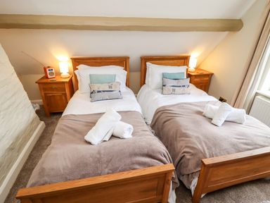 A bedroom with two single beds each with folded towels bedside tables with lamps and a radio at Damson Cottage in Whitby