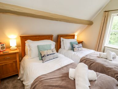 A bedroom with two single beds bedside tables lamps and window at Damson Cottage in Whitby