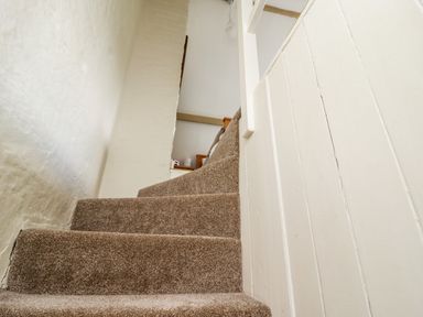 A carpeted staircase with white walls and wooden handrail at Damson Cottage in Whitby