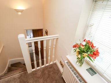 A stairway landing with carpeted stairs a white banister a vase of flowers on a windowsill with blinds and a radiator below at Damson Cottage in Whitby