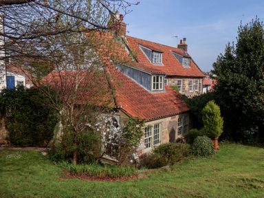 A two-story house with red tiled roofs surrounded by trees and shrubs at Damson Cottage in Whitby