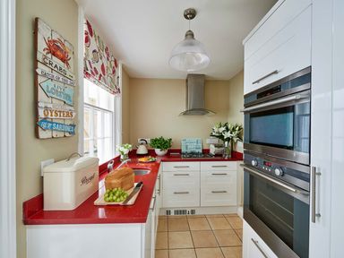 A kitchen with red countertops white cabinets built in oven bread box and a window at Harbour House in Whitby