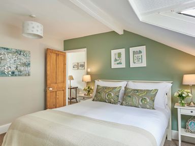 A bedroom with a bed against a green wall with two pillows and two framed pictures two bedside tables with lamps and flowers and an open wooden door at Harbour House in Whitby