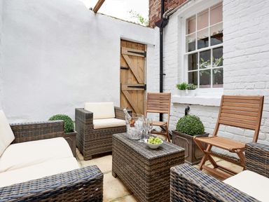 An outdoor patio with wicker sofas and wooden chairs around a wicker table holding a bowl of grapes and glasses at Harbour House in Whitby