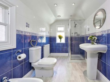 A bathroom with a toilet, pedestal sink, glass shower enclosure, and flowers in a vase at Harbour House in Whitby