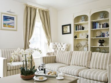 A sitting room with striped sofas, a coffee table with tea and scones, bookshelves, and curtains at Albany House Whitby