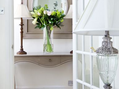 A hallway with a console table holding a vase of flowers and a lamp with a mirror above the table at Albany House Whitby