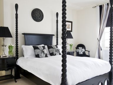 A bedroom with a black four-poster bed white bedding black and silver decorative pillows two black nightstands with silver lamps and flowers black chair with pillow and window with curtains at Albany House Whitby