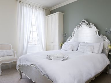 A bedroom with a silver ornate bed frame white bedding white curtains a wardrobe and a chair at Albany House Whitby