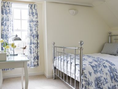 A bedroom with a metal bed, patterned bedding, a window with curtains, and a desk with a lamp and flowers at Albany House Whitby