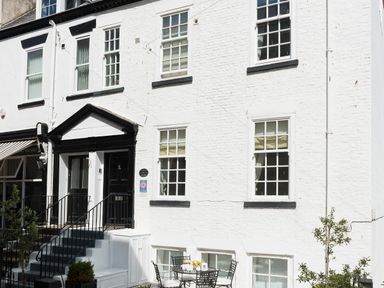 Exterior of a white brick building with black and white entrance door black metal staircase and outdoor metal table with chairs at Albany House Whitby