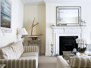 A living room with striped sofas a model sailboat on a side table a fireplace with a large mirror above and a coffee table with tea set and flowers at Albany House Whitby