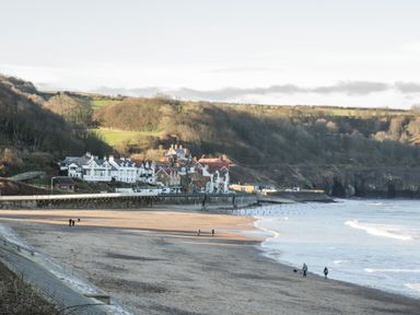A beach with people walking near the shore and houses along a coastal road at The Cottage in Sandsend