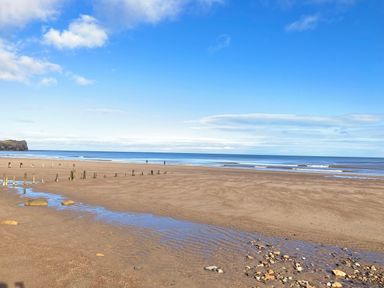 A sandy beach with wooden posts and small rocks near the shoreline at The Cottage in Sandsend