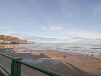 A beach with people walking near the shore and cliffs in the background at The Cottage in Sandsend