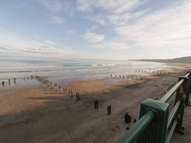 A beach with wooden posts in the sand and a railing in the foreground at The Cottage in Sandsend
